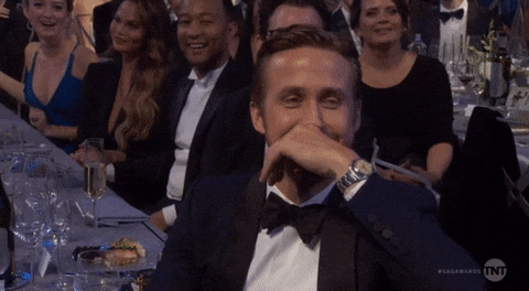 Celebrity gif. Ryan Gosling at the SAG Awards in 2017. He's sitting at a table and he cracks up, rubbing his brow and covering his mouth with his hand as he laughs.