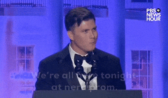 Video gif. Saturday Night Live's Colin Jost stands at a podium at the 2024 White House Correspondents' Dinner and delivers a joke. He says, "We're all here tonight at nerd prom" and pauses for a moment. He then says "Well, Matt Gaetz is at regular prom."