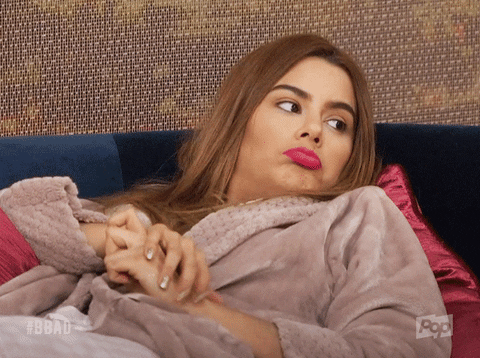 Reality TV gif. A woman on Big Brother lays back on a sofa in a bathrobe and shrugs. 