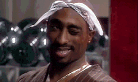 Celebrity gif. Tupac wears a white bandana tied around his head as he smiles and winks to the side.
