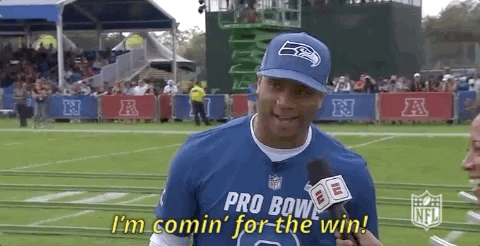 Sports gif. Russell Wilson speaks into a microphone and backs away from reports as he says, “I’m comin’ for the win!”