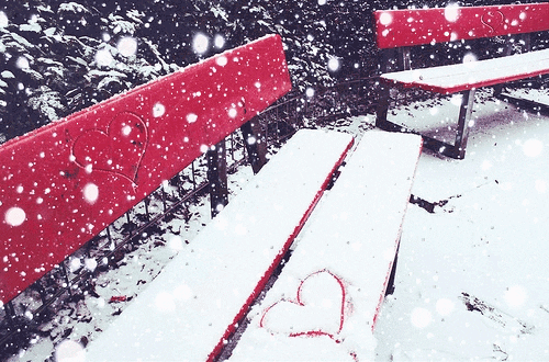 Photo gif. Two red benches covered with a layer of snow; the foreground bench has a heart drawn in the snow.