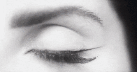 Music video gif. Close-up of an eye slowly opening, reflecting many lights from a starry sky or galaxy, from Lana Del Rey's video for "Lust for Life."