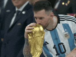 Sports gif. Lionel Messi rubs the World Cup trophy and gives it a gentle, slow kiss. He smiles and rubs and kisses it again.