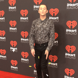 Celebrity gif. Trevi Moran stands on the red carpet at the iHeart Festival in 2016. Sparkles animate over the screen as she puts both of her hands to her face and blows a kiss to us, seeming to mouth, "Muah."