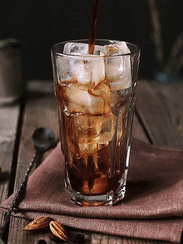 Video gif. Coffee pours into a glass full of ice cubes.