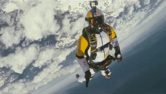 Video gif. A skydiver hovers in the air and gives someone a high five before turning and floating away.