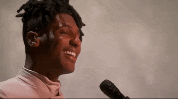 Oscars 2024 GIF. Close up shot of Jon Batiste finishing up his performance of "Never Went Away" from American Symphony. He leans away form the microphone, smiling at the crowd and nodding his head.