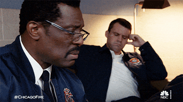 TV gif. Eamonn Walker as Wallace Boden on Chicago Fire sits on a couch next to Jesse Spencer as Matthew Casey. Wallace turns to look at Matthew. Matthew looks around as if trying to figure out an answer and then shrugs.