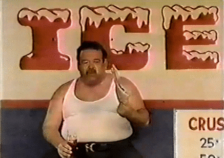 Video gif. Man is sitting in front of an ice sign holding a soda and is fanning himself with a pamphlet, trying to beat the heat.