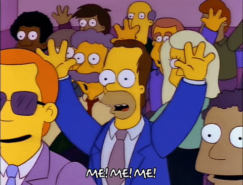 The Simpsons gif. A young Homer Simpson sits in a crowd, wearing a suit. He raises his hand and points to himself with his other hand, shouting, "Me! Me! Me!"