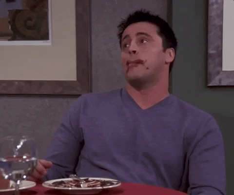 Friends gif. Matt LeBlanc as Joey licks his chocolate-smeared lips as he leans back from a table with innocent eyes.