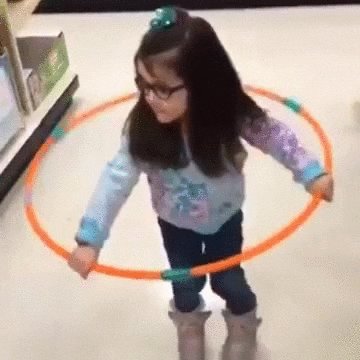 Video gif. A young girl at a store attempts to hula hoop but fails, the hula hoop dropping to the floor. She keeps wiggling her hips as if she is hula hooping. She picks the hoop back up and tries again, then fails again, wiggling in vain.