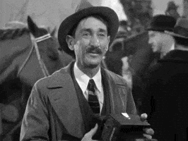 Movie gif. Photographer from an Alfred Hitchcock film is about to take a photo of someone and he looks pleased as he sees the subject's pose and says, "That's very good!"