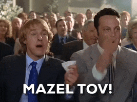 Movie gif. Owen Wilson as John and Vince Vaughn as Jeremy in Wedding Crashers genuinely cheering with the rest of the crowd at some big wedding moment. Text, "Mazel Tov!"