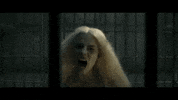 Movie gif. Margot Robbie as Harley Quinn in Suicide Squad runs towards us in her large cage-like jail cell. She screams and then bangs her head straight into the metal bar.