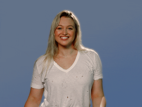 Video gif. Iskra Lawrence makes a heart shape with her fingers in front of her chest as she shimmies down with a squint and a smile before pointing at us with both hands.