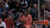 Sports gif. Bam Adebayo and RJ Hampton of the Miami Heat are sitting on the bench and they're cracking up laughing. They hold on to each other busting up as they stomp their feet.