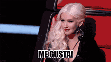 Reality TV gif. On The Voice, Christina Aguilera smiles flirtingly and bobs her head rhythmically. Text, in Spanish, reads, "Me gusta!"