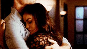 TV gif. A couple shares a hug. A shorter woman rests her head on the chest of a taller man, who places a hand on her head and kisses her.