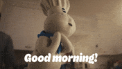 Sponsored gif. Pillsbury Doughboy spins happily while people around him eat breakfast. Text reads, "Good morning!"