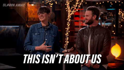 Reality TV gif. Katherine Burns and Bobby Berk, the judges of Blown Away, stand in front of the contestants chuckling. Katherine says, "This isn't about us. This is about you." 
