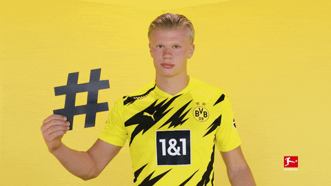 Sports gif. Soccer player Erling Haaland points at a paper he is holding with a big hashtag on it.