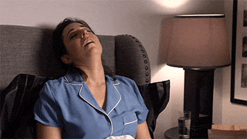 Video gif. A woman in a chair sleeps deeply as her head tilts back in exhaustion. 