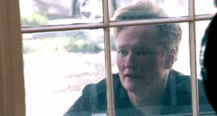 Late Night gif. Conan O'Brien looking in through a window, hand to the glass in a gesture of longing.
