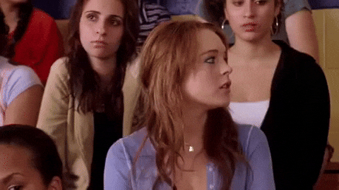 Movie gif. Sitting on bleacher seats with other students, Lindsay Lohan as Cady in Mean Girls looks to the side, raises her hand and waves her fingers.