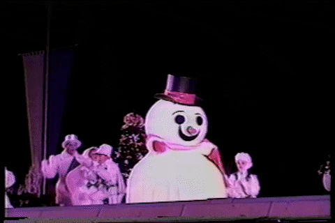 Video gif. A big snowman mascot hops across a concert stage as children dance behind it. The snowman accidentally falls off the side and into the band pit. 