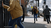 TV gif. A woman wearing a badge in Chicago PD runs down a city sidewalk with a badge hanging from her jeans as people around her run away in the opposite direction.