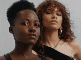 Celebrity gif. Lupita Nyong'o and Zendaya gaze at us as they slowly turn their face and shoulders as they model in a photoshoot.