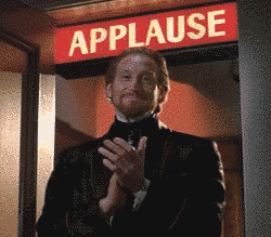 Video gif. A clapping man stands under a sign that’s flashing the word, “applause.”