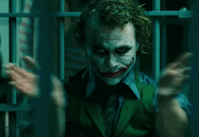 Movie gif. Heath Ledger as the Joker inside of a cage, looking up with a slight smirk and clapping his hands.