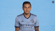 Sports gif. Ronald Matarrita from NYCFC is wearing his soccer jersey and he smiles softly as he shrugs his shoulders nonchalantly.