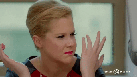 TV gif. Amy Schumer on Inside Amy Schumer holds her hands up in a shrug as she squints and chews with confusion on her face.