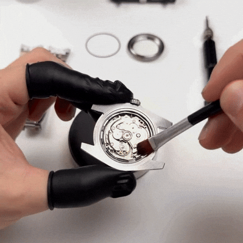 Watchmaker cleaning a mechanical watch movement with a brush.