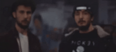Video gif. Two men stare at us very seriously. A fire then comes into view in front of them.