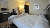 Video gif. From the foot of a bed, a shirtless man does a backflip onto the bed, then flips onto his back smoothly and pulls the covers over him.
