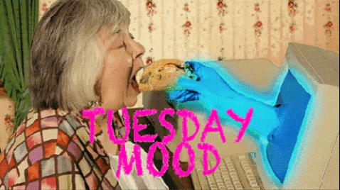 Meme gif. Older woman takes a passionate bite of a taco, held out in front of her by a blue-gloved hand bursting out of an old computer screen. Text, "Tuesday mood."
