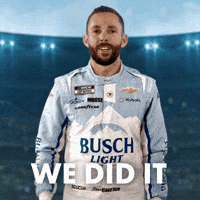 Sponsored gif. NASCAR driver Ross Chastain smiles and holds his fist in the air in triumph. He wears a driver fire suit decorated with many sponsor logos with the largest being the Busch Light beer logo across the center of his abdomen. Text reads, “We did it.”