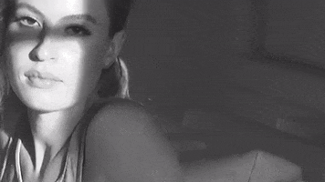 Music video gif. From Fletcher's video for "Sex With My Ex," black and white video zooms in on the face of a girl who looks to the side, seemingly annoyed, and then zooms in toward her breasts.