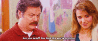 Parks and Recreation gif. Nick Offerman as Ron squints with suspicion while speaking, while Lucy Lawless as Diane looks on with a subtle smile. Text, "Are you dead? You look like you're in rictus."