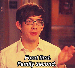 TV gif. Kevin McHale as Artie Abrams in Glee sits in a white polo and wears black glasses. He holds his hand out in front of him, then moves it to the side. Text reads, "Food first. Family second."
