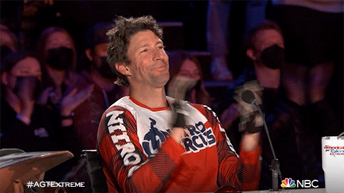 TV gif. Travis Pastrana from America's Got Talent: Extreme sits back in his chair, proudly clapping and grinning.