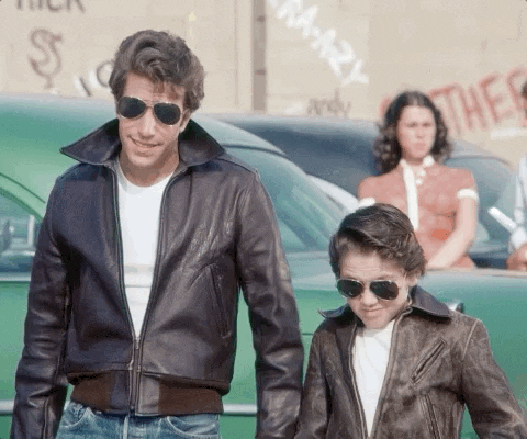 TV gif. Henry Winkler as The Fonz wears his signature pompadour, leather bomber jacket and aviators, standing next to a young kid also wearing a pompadour, leather bomber jacket and aviators. They both give us a thumbs up.