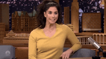 Late Night gif. Sarah Silverman shrugs awkwardly, stiffly moving her arms around exaggeratedly.