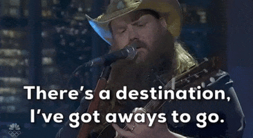 Video gif. Saturday Night Live castmember Mikey Day and guest host Ryan Gosling are dressed as Beavis and Butt-head for a sketch. Day and Gosling are sitting in the front row of a talk show audience. The two of them are staring straight ahead with goofy smiles on their faces. 