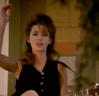 Celebrity gif. With a guitar strapped over her shoulder, Shania Twain points at us.